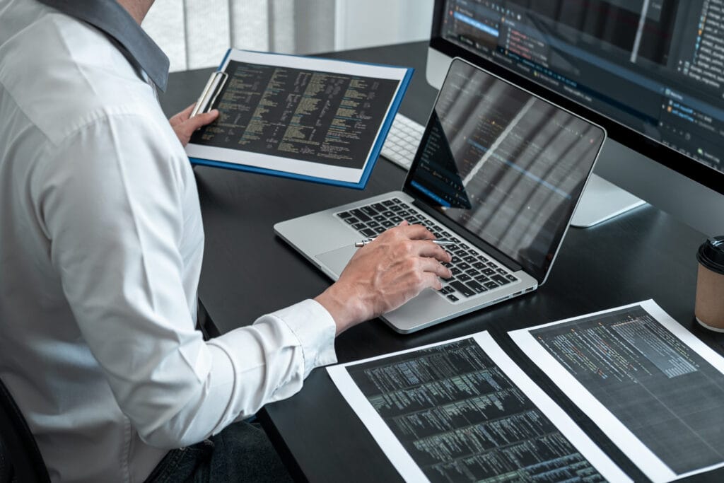 Male programmer working on a data science project in software development on the desktop computer and making coding and typing data code.