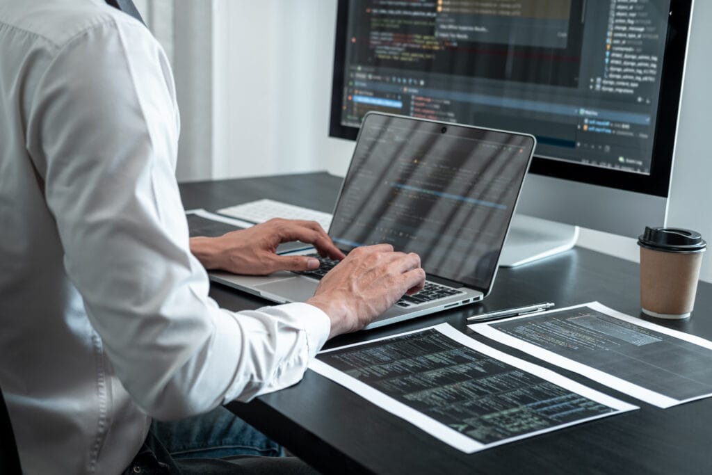 Male programmer working on a data science project in software development on the desktop computer and making coding and typing data code.