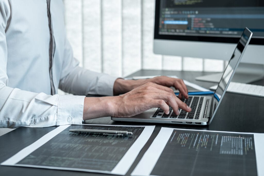Male programmer working on a data science project in software development on the desktop computer and making coding and typing data code.