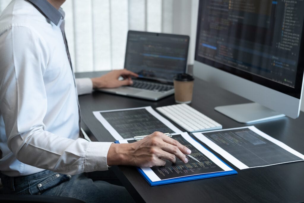 Male programmer working on another data science project in software development on the desktop computer and making coding and typing data code.