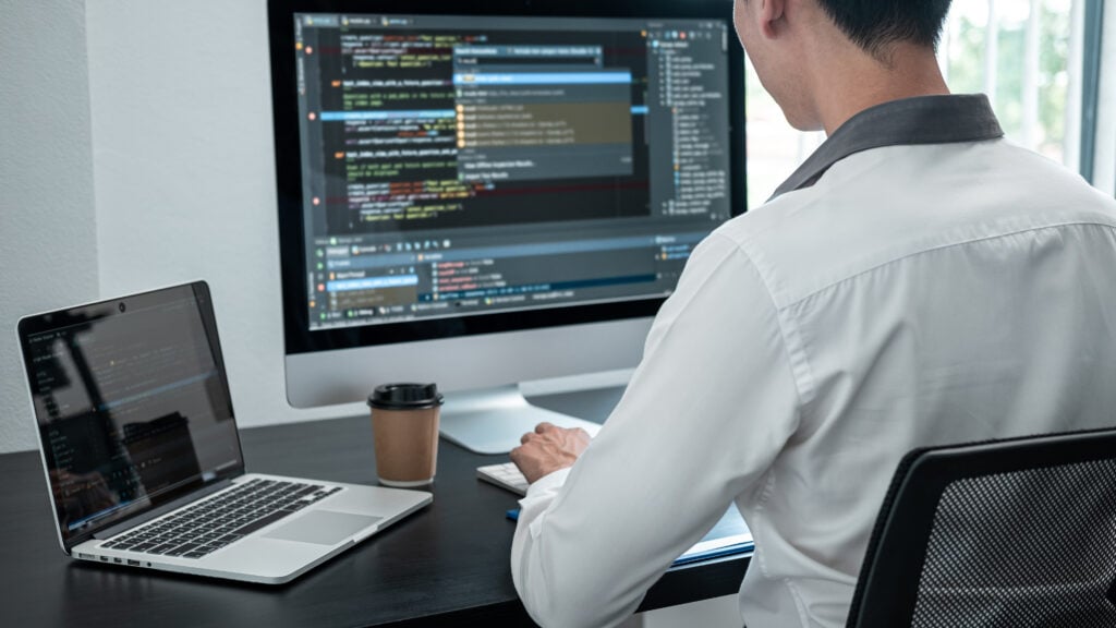 Male programmer working on a data science project on the desktop computer and making coding and typing.